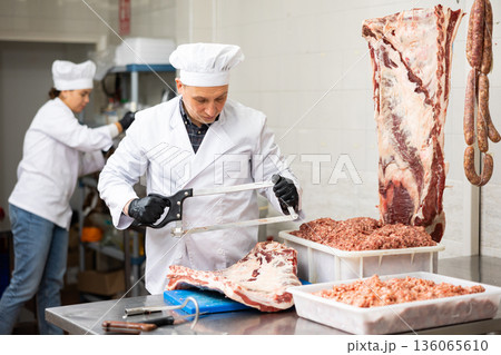 Happy female butcher sawing big chunk of beef meat in meat section of supermarket Happy female butcher sawing big chunk of beef meat in meat section of supermarket 136065610