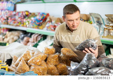 Man carefully choice raisin and other dried fruits in grocery store Man carefully choice raisin and other dried fruits in grocery store 136065613