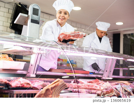 Happy female butcher holding big chunk of beef meat in meat section of supermarket 136065619