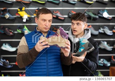 Father and son together choose and buy winter sports shoes for hiking in sports store Father and son together choose and buy winter sports shoes for hiking in sports store 136065707