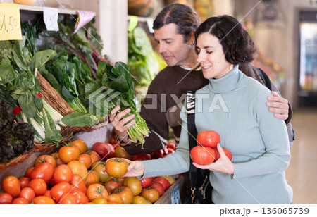 Married couple selects fresh bell peppers, tomatoes and other vegetables at supermarket counter 136065739