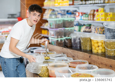 Interested guy filling poly bag with pickled olives in food store 136065741