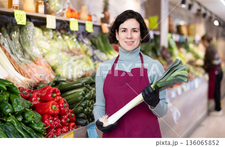 Adult woman seller with leeks in vegetable shop 136065852