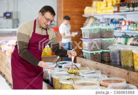 Frienfly male supermarket grocery seller offers to buy pickled green olives Frienfly male supermarket grocery seller offers to buy pickled green olives 136065868