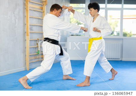 Underage boy and middle-aged man performing karate techniques in pair 136065947