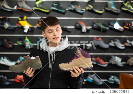 Interested male athlete chooses sports winter shoes for hiking in sports store Interested male athlete chooses sports winter shoes for hiking in sports store 136065982