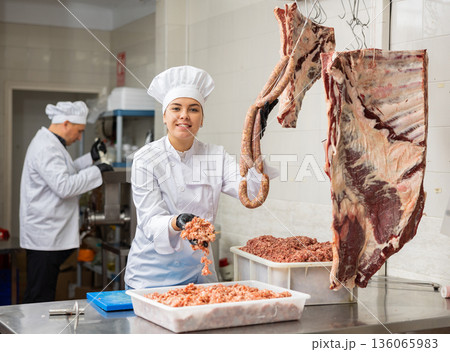 Female butcher offering raw sausages made of fresh forcemeat Female butcher offering raw sausages made of fresh forcemeat 136065983