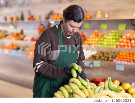 Adult man seller puts bananas on display Adult man seller puts bananas on display 136066021