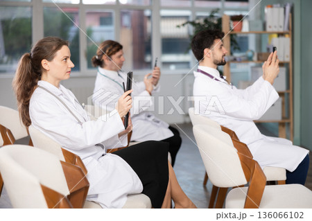 Medical students or doctors using mobile phones to scan QR-code during interactive lesson Medical students or doctors using mobile phones to scan QR-code during interactive lesson 136066102