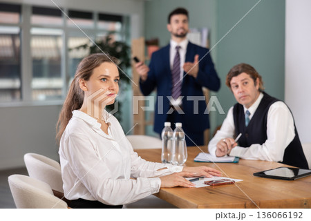 Business partners sitting at table and chatting, colleague with remote control telling at background 136066192