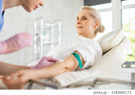 Old woman patient having vein injection lying on clinical chair 136066272