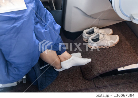Inflight business class passenger with ample leg room took off shoes during flight for comfort travel 136067394