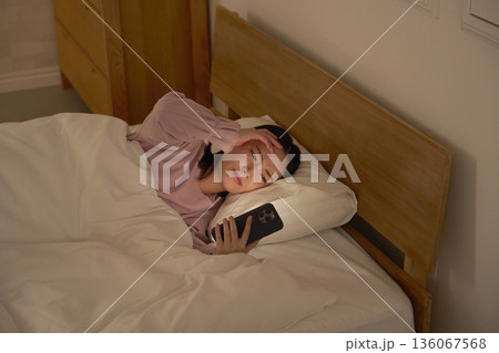 布団の中でスマホを見る女性 136067568