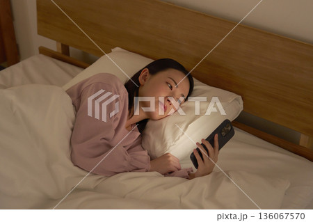 布団の中でスマホを見る女性 136067570