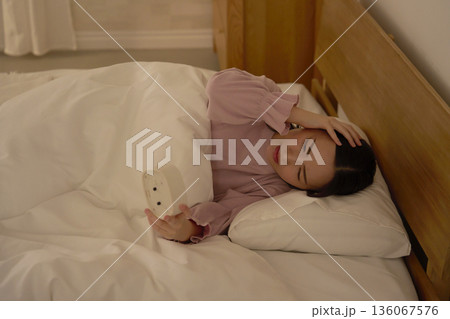深夜に布団の中で時計を見ている女性 136067576