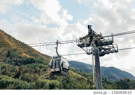 A cable car station in the mountains. The structure is supported by a tall pole, surrounded by lush green hills and a cloudy sky. Ideal for vacation activities 136068610