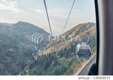cable car travels up a mountain slope. The landscape features rocky terrain and trees. The sky is clear with soft clouds, indicating a pleasant vacation atmosphere. cable car travels up a mountain slope. The landscape features rocky terrain and trees. The sky is clear with soft clouds, indicating a pleasant vacation atmosphere. 136068615