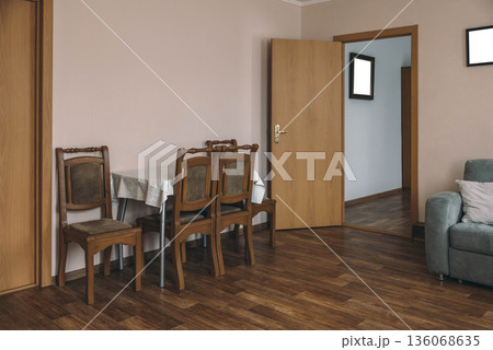A cozy hotel room with wooden flooring. A small dining table with four chairs is set against a light pink wall. A door leads to another room, and a sofa is visible. A cozy hotel room with wooden flooring. A small dining table with four chairs is set against a light pink wall. A door leads to another room, and a sofa is visible. 136068635
