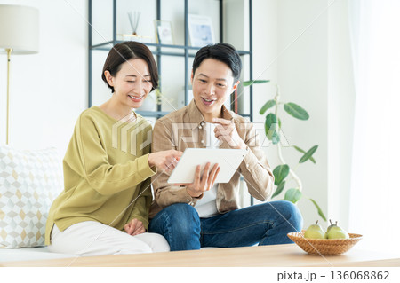 リビングでタブレット端末を使うミドルの夫婦 リビングでタブレット端末を使うミドルの夫婦 136068862