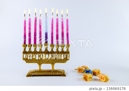 Menorah with lit candles stands on table while spinning tops are nearby as part of Hanukkah holiday event. 136069176