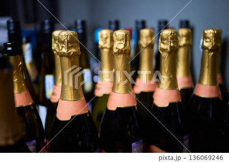 Rows of champagne bottles, gold foil, pink labels, closeup retail shelf, blurred background, warm highlights, premium texture, celebratory mood, event preparation, upscale party Rows of champagne bottles, gold foil, pink labels, closeup retail shelf, blurred background, warm highlights, premium texture, celebratory mood, event preparation, upscale party 136069246