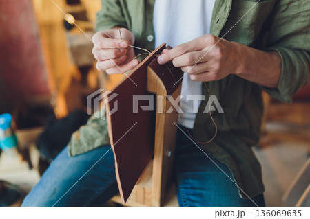 Handcrafted leather journal. Focused image of homemade leather book being handcrafted. Intimate view of skilled craftsman sewing waxed thread onto brown leather journal Handcrafted leather journal. Focused image of homemade leather book being handcrafted. Intimate view of skilled craftsman sewing waxed thread onto brown leather journal 136069635