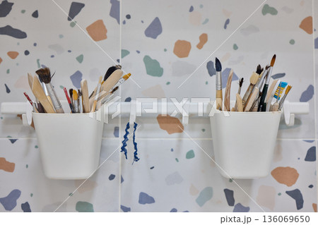 Terrazzo wall with organized brushes, Minimalist craft room featuring hanging pots with brushes, Clean design showcasing studio tools against neutral terrazzo background setting Terrazzo wall with organized brushes, Minimalist craft room featuring hanging pots with brushes, Clean design showcasing studio tools against neutral terrazzo background setting 136069650