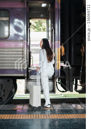 Woman in a white suit with luggage boarding a train, ready for a travel adventure at a station platform. Woman in a white suit with luggage boarding a train, ready for a travel adventure at a station platform. 136069711