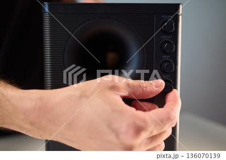 Adjusting bass knob in listening space, Technician modifies subwoofer settings in cozy setup, Close examination of audio equipment controls under warm lighting conditions 136070139