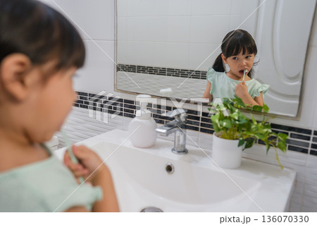 girl child brushing teeth at reflection in mirror in bathroom 136070330