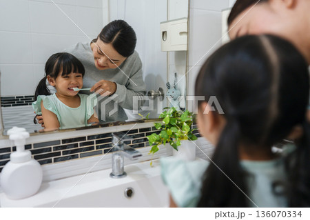 mother teaching girl child to brushing teeth at reflection in mirror in bathroom 136070334