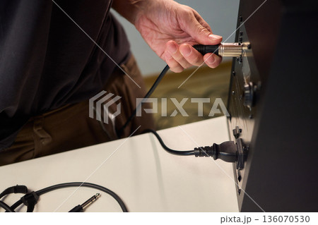 Setting up audio connection professionally, Attaching sound cable to subwoofer in studio, Closeup of hands securing audio cable into subwoofer in recording studio setting Setting up audio connection professionally, Attaching sound cable to subwoofer in studio, Closeup of hands securing audio cable into subwoofer in recording studio setting 136070530