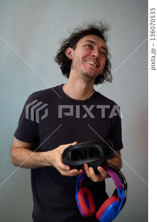 Happy guy with headphones, Casual man showcases vibrant headphones, Casually dressed man with curly hair showcases playful headphones during informal indoor photography session 136070535