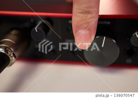 Adjusting audio controls, Precise handling of control knobs on audio equipment during setup, Fingers align control dials on audio interface for optimal sound calibration Adjusting audio controls, Precise handling of control knobs on audio equipment during setup, Fingers align control dials on audio interface for optimal sound calibration 136070547