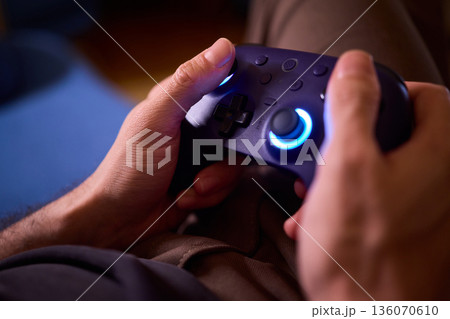 Comfortable man enjoying gameplay under colorful neon illumination, Chill indoor scene featuring smiling individual engaged in video game entertainment amid vivid purple lights 136070610