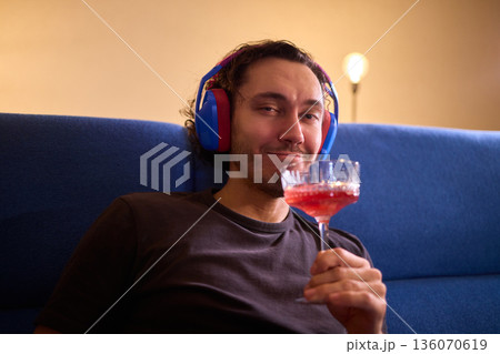 Relaxed man enjoying wine, Person wearing headphones rests peacefully, Creative professional enjoys evening relaxation with wine and soothing music in modern living space 136070619