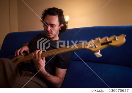 Musician working in cozy studio, Casual musician practicing bass with effects and accents, Relaxed bassist intensely rehearsing in warmly lit home recording environment 136070627