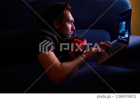 Casual night working from comfy sofa, Quiet evening spent on freelance project in cozy living room, Man enjoying late night work at home with relaxed posture and soft glow Casual night working from comfy sofa, Quiet evening spent on freelance project in cozy living room, Man enjoying late night work at home with relaxed posture and soft glow 136070652