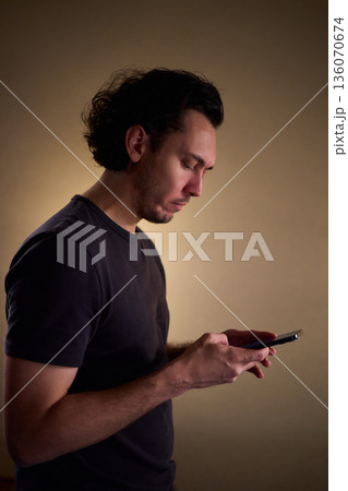Chilled man on sofa, Casual individual reclining on sofa engrossed with mobile device, Unwinding man sits comfortably on sofa focused on his smartphone amid cozy modern decor 136070674