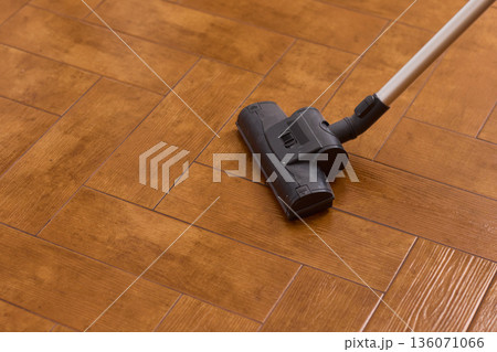 Hardwood floor vacuum head gliding across polished parquet, closeup of nozzle brushing wood grain, warm lighting, quiet household cleaning, gentle maintenance mood 136071066