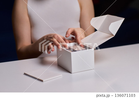 Closeup of hands opening clean packaging under controlled lighting. Lifestyle marketing shot emphasizing tactile clarity while revealing unbranded box in refined setting Closeup of hands opening clean packaging under controlled lighting. Lifestyle marketing shot emphasizing tactile clarity while revealing unbranded box in refined setting 136071103