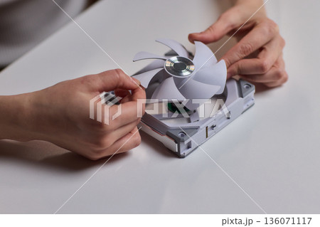 DIY fan repair. Hand fixing plastic fan blades. Closeup of assembling fan blades by hand. Engaging image of hands carefully attaching white blades onto motor hub for repair 136071117