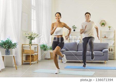 Fit couple doing cardio workout together at home, high knees and smiles indoors Fit couple doing cardio workout together at home, high knees and smiles indoors 136071394