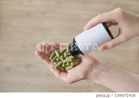 Women's hand dispensing green capsules from blank supplement bottle 136071416