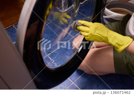 Washing glass door carefully now, Household cleaning of washing machine glass, Performing hygienic maintenance with circular motions on washing machine door glass Washing glass door carefully now, Household cleaning of washing machine glass, Performing hygienic maintenance with circular motions on washing machine door glass 136071462