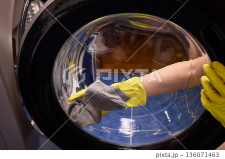 Washing glass door carefully now, Household cleaning of washing machine glass, Performing hygienic maintenance with circular motions on washing machine door glass Washing glass door carefully now, Household cleaning of washing machine glass, Performing hygienic maintenance with circular motions on washing machine door glass 136071463