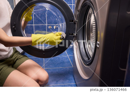 Washing glass door carefully now, Household cleaning of washing machine glass, Performing hygienic maintenance with circular motions on washing machine door glass Washing glass door carefully now, Household cleaning of washing machine glass, Performing hygienic maintenance with circular motions on washing machine door glass 136071466