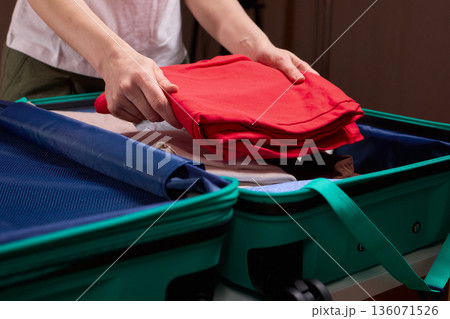 Organizing clothes before travel, Traveler arranges garments meticulously in their suitcase, An individual smoothly folds clothing and organizes suitcase for upcoming departure 136071526