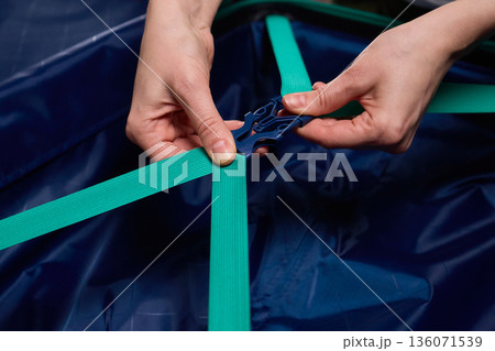 Hands tightening teal travel luggage strap, Closeup of hands attaching teal strap to luggage, Detailed shot of hands securing bright teal bag strap during travel preparation Hands tightening teal travel luggage strap, Closeup of hands attaching teal strap to luggage, Detailed shot of hands securing bright teal bag strap during travel preparation 136071539