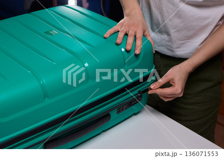 Traveler opening luggage, Close shot of hands unfastening suitcase zipper before travel, Detailed view of hands pulling zipper on vibrant teal travel case with anticipation Traveler opening luggage, Close shot of hands unfastening suitcase zipper before travel, Detailed view of hands pulling zipper on vibrant teal travel case with anticipation 136071553